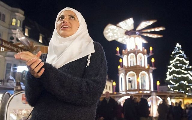 Syrian refugee Reem Habashieh stands in front of a Christmas traditional wooden pyramid at the Christmas market in Zwickau, eastern Germany on Tuesday, Dec. 8, 2015. (AP Photo/Jens Meyer)