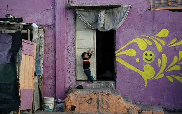 In this Saturday Dec. 19, 2015 photo, a Palestinian boy hangs on a door of his home that was painted by artists in the Shati refugee camp in Gaza City. (AP Photo/Hatem Moussa)