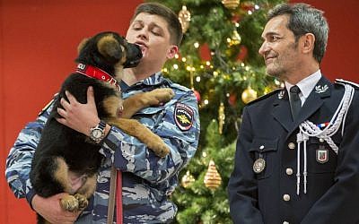 A Russian police officer holds a puppy, named Dobrynya, as a French police officer smiles before presenting the puppy to French police in the French Embassy in Moscow, Russia, Monday, December 7, 2015. (AP/Pavel Golovkin)