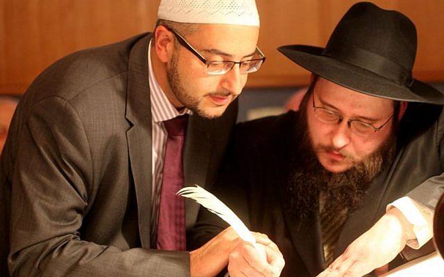 Dr. Bilal El-Zayat (left), leader of the Muslim community of Marburg, Germany, helps Josef Chranovsky write one of the final letters in a new Torah scroll, November 29, 2015. (Rainer Waldinger/Jüdische Gemeinde Marburg)