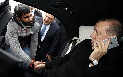 Turkish President Recep Tayyip Erdogan, right, takes Vezir Cakras by hand while speaking on his mobile phone inside his car stationed over the Bosporus Bridge in Istanbul, Friday, Dec. 25, 2015. Erdogan’s office says the Turkish president has talked Cakras out of jumping off a bridge to commit suicide. (Yasin Bulbul/Presidential Press Service Pool via AP Photo)