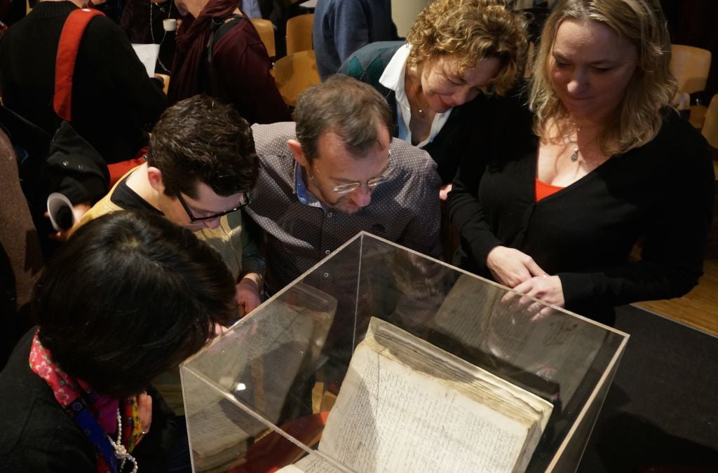 Attendees at an Amsterdam symposium on whether to lift the ancient order of excommunication against the philosopher Baruch Spinoza examining a copy of the original writ against him, December 6, 2015 (Cnaan Liphshiz/JTA) Attendees at an Amsterdam symposium on whether to lift the ancient order of excommunication against the philosopher Baruch Spinoza examining a copy of the original writ against him, December 6, 2015 (Cnaan Liphshiz/JTA)