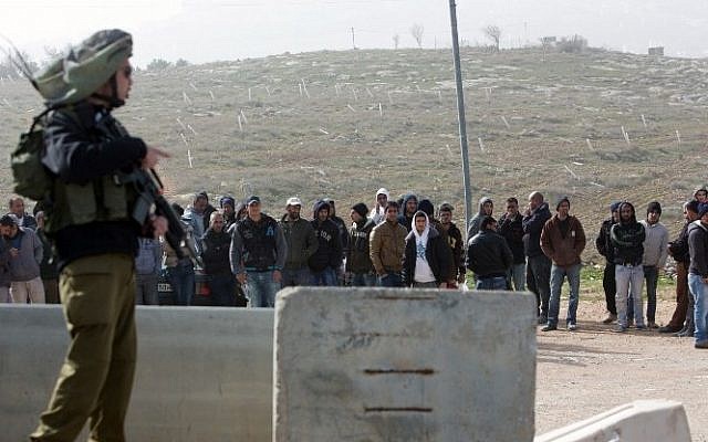 An Israeli soldier stands guard next to Palestinian workers who were transported out of the Tekoa settlement south of Jerusalem following a terror attack in the community on January 18, 2016. (AFP / MENAHEM KAHANA)
