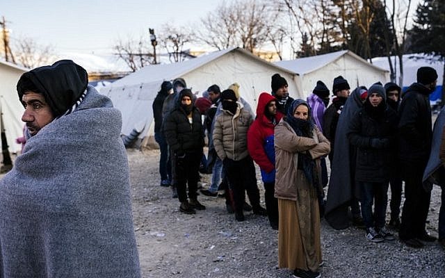A migrant wrapped in a blanket waits with other migrants and refugees for a bus at a registration camp in southern Serbian town of Presevo on January 20, 2016, as temperature fall to minus 15 Celsius. (AFP/DIMITAR DILKOFF)