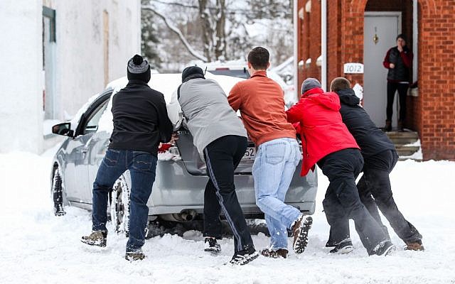 A group of friends help push a car into a safe parking spot after it was stuck on a snow-covered road in Huntington, West Virginia. (Sholten Singer/The Herald-Dispatch via AP)