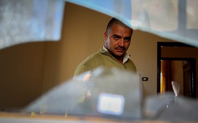 A Palestinian man stands near the broken window of a house that was sprayed with graffiti reading "revenge" and "hello from the prisoners of Zion", in a suspected Jewish terror attack in the village of Beitillu, near Ramallah in the West Bank on December 22, 2015. (Flash90)