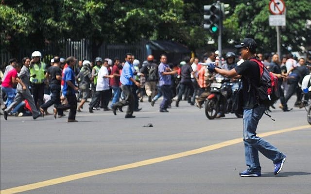 In this photo released by China's Xinhua News Agency, an unidentified man with a gun walks in the street as people run in the background on Thamrin street near Sarinah shopping mall in Jakarta, Indonesia, Thursday, January 14, 2016. (Veri Sanovri/Xinhua via AP)