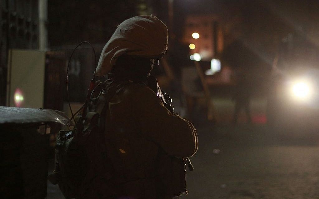 A soldier stands guard in the light of an army jeep in Qalqilya on January 14, 2016. (Judah Ari Gross/Times of Israel/File)