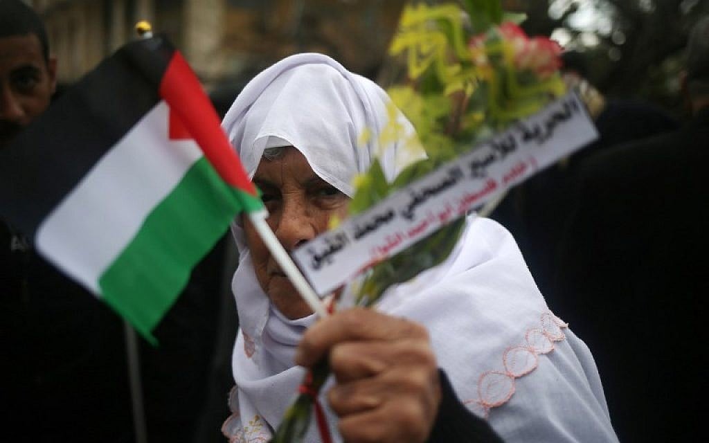 A Palestinian woman holds flowers and her national flag during a demonstration in support of hunger striking Palestinian journalist Mohammed al-Qiq, on February 8, 2016, in Gaza City. (AFP / MOHAMMED ABED)