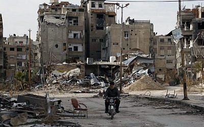 A man drives his motorbike past damaged apartment buildings on February 10, 2016 in Harasta, east of the Syrian capital Damascus (AFP / ABDULMONAM EASSA)