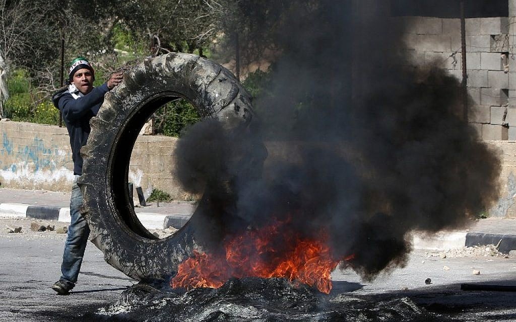 A Palestinian demonstrator places a tire onto a fire during clashes with Israeli borderguards in the village of Araka on February 15, 2016. (AFP/JAAFAR ASHTIYEH)