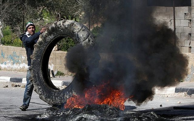 A Palestinian demonstrator places a tire onto a fire during clashes with Israeli borderguards in the village of Araka on February 15, 2016. (AFP/JAAFAR ASHTIYEH)