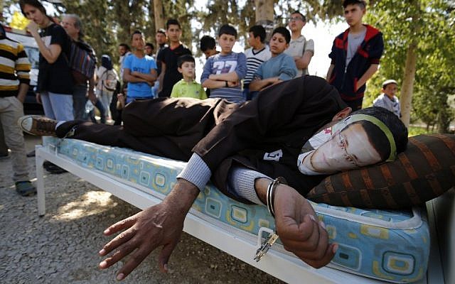 A Palestinian man lying on a bed wears a mask depicting hunger-striking Palestinian journalist Mohammed al-Qiq during a demonstration in solidarity with him in the West Bank village of Bilin, February 19, 2016. (AFP/Abbas Momani) A Palestinian man lying on a bed wears a mask depicting hunger-striking Palestinian journalist Mohammed al-Qiq during a demonstration in solidarity with him in the West Bank village of Bilin, February 19, 2016. (AFP/Abbas Momani)
