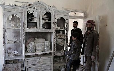 Syrians stand next to a sideboard covered with dust as they collect items in the buildings that were left behind by residents fleeing violence on February 27, 2016 in the rebel-held town of Douma, on the eastern edges of the capital Damascus. (AFP/AMER ALMOHIBANY)