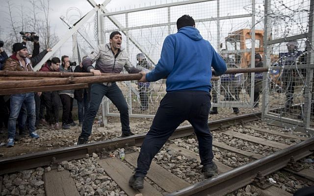 Refugees and migrants try to break an iron fence from the Greek side of the border as Macedonian police stand guard, near the northern Greek village of Idomeni on Monday, February 29, 2016. (AP/Petros Giannakouris)