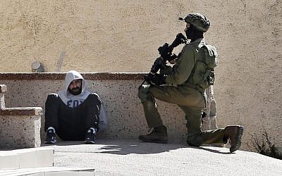 In this Feb. 15, 2016 file photo, an Israeli soldier keeps guard by an arrested Palestinian man at the Amari refugee camp, near the West Bank city of Ramallah. (AP Photo/ Nasser Shiyoukhi, File)