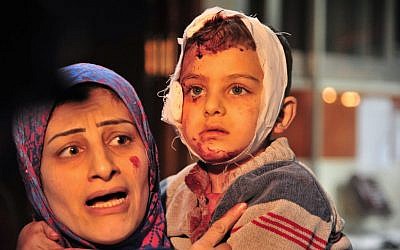 In this photo released by the Syrian official news agency SANA, a woman carries a child injured in the triple blast in Sayyida Zeinab, a predominantly Shiite Muslim suburb of the Syrian capital Damascus arrives to a hospital to receives treatment, Syria, Sunday, Feb. 21, 2016. (SANA via AP)