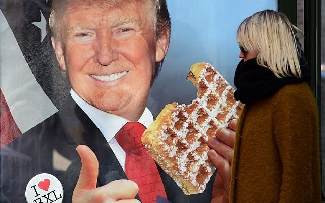 A woman walks by a bus stop with an advertisement campaign for a Belgium radio news channel picturing US presidential candidate Donald Trump eating a waffle, in reference to Trump calling Brussels a hellhole, due to the amount of its Muslim population, on February 29, 2016 in Brussels. (AFP / EMMANUEL DUNAND)