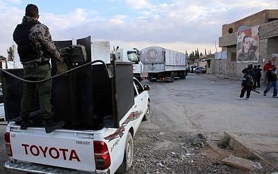 A militiaman, loyal to the Syrian regime forces, stands guard as an aid convoy of the Syrian Red Crescent crosses the Syrian army checkpoint at al-Wafideen refugee camp on the Damascus-Douma road before delivering aid to three cities in the rebel bastion of Eastern Ghouta on March 4, 2016. (AFP/YOUSSEF KARWASHAN)