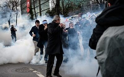 Men run and cover their faces as Turkish anti-riot police officers use tear gas to disperse supporters in front of the headquarters of the Turkish daily newspaper Zaman in Istanbul on March 5, 2016, after Turkish authorities seized the headquarters in a midnight raid. (AFP/OZAN KOSE)