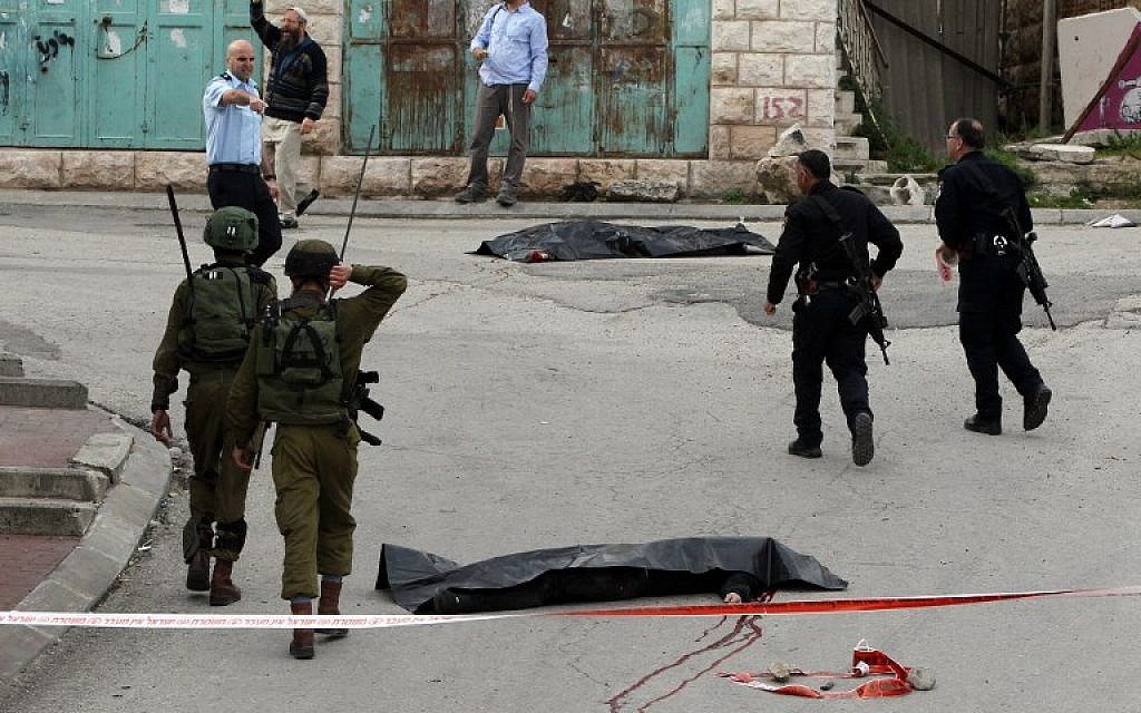 Israeli soldiers and police surround the bodies of two Palestinians who had wounded an Israeli soldier in a knife attack in the West Bank city of Hebron, March 24, 2016. (AFP/Hazem Bader)
