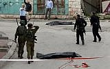Israeli soldiers and police surround the bodies of two Palestinians who had wounded an Israeli soldier in a knife attack in the West Bank city of Hebron, March 24, 2016. (AFP/Hazem Bader)