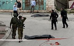 Israeli soldiers and police surround the bodies of two Palestinians who had wounded an Israeli soldier in a knife attack in the West Bank city of Hebron, March 24, 2016. (AFP/Hazem Bader)