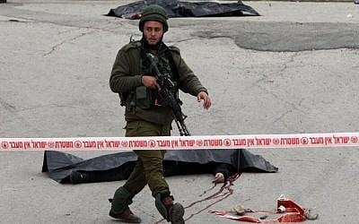 An Israeli solider guards the bodies of two Palestinians who were killed after wounding an Israeli soldier in a knife attack before being shot dead by troops on March 24, 2016 (AFP / HAZEM BADER)