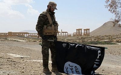 A member of the Syrian pro-government forces carries an Islamic State flag as he stands on a street in the ancient city of Palmyra on March 27, 2016, after troops recaptured the city from IS jihadists. (AFP/STR)