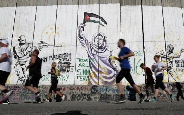Participants run along Israel's security barrier in the West Bank town of Bethlehem during the 4th Palestine Marathon on April 1, 2016. (AFP / THOMAS COEX)