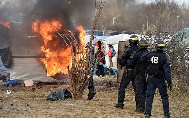 Anti-riot policemen stand near a shack burning during the dismantling of half of the "Jungle" migrant camp in the French northern port city of Calais, on February 29, 2016. (AFP PHOTO / PHILIPPE HUGUEN) Anti-riot policemen stand near a shack burning during the dismantling of half of the "Jungle" migrant camp in the French northern port city of Calais, on February 29, 2016. (AFP PHOTO / PHILIPPE HUGUEN)
