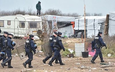 Policemen walk as people stand on a shelter's roof on  March 1, 2016 in the 'Jungle' migrants and refugees camp in the French northern port city of Calais during the dismantling of half of the camp. (AFP/Philippe Huguen)