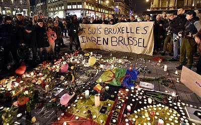 People holding a banner reading "I am Brussels" behind flowers and candles to mourn for the victims at Place de la Bourse in the center of Brussels, Tuesday, March 22, 2016. (AP Photo/Martin Meissner)