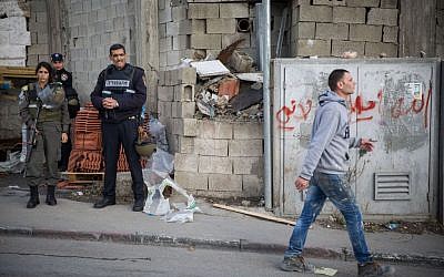 Illustrative: A Palestinian man walks past Israeli police officers at the entrance to the Shuafat refugee camp in East Jerusalem on December 2, 2015. (Hadas Parush/Flash90)