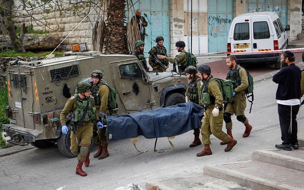 Israeli soldiers remove the body of a Palestinian man shot after he stabbed and wounded a soldier in the West Bank city of Hebron on March 24, 2016. (Wissam Hashlamon/Flash90)