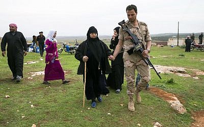 In this photo taken on Wednesday, March 2, 2016, a Syrian solder helps an elderly woman as she comes to receive humanitarian aid from Russian military near Maarzaf, about 15 kilometers west of Hama, Syria. (AP Photo/Pavel Golovkin) 