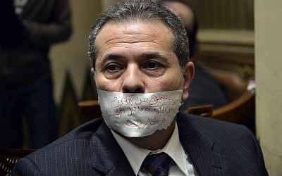 In this Jan. 12, 2016 file photo, MP Tawfiq Okasha sits in an anteroom after he taped his mouth shut in protest at not being given the floor during a parliamentary session, in Cairo, Egypt. Arabic writing reads, "Banned from speaking inside and outside the house by government orders." (AP Photo/Said Shahat, File) In this Jan. 12, 2016 file photo, MP Tawfiq Okasha sits in an anteroom after he taped his mouth shut in protest at not being given the floor during a parliamentary session, in Cairo, Egypt. Arabic writing reads, "Banned from speaking inside and outside the house by government orders." (AP Photo/Said Shahat, File)