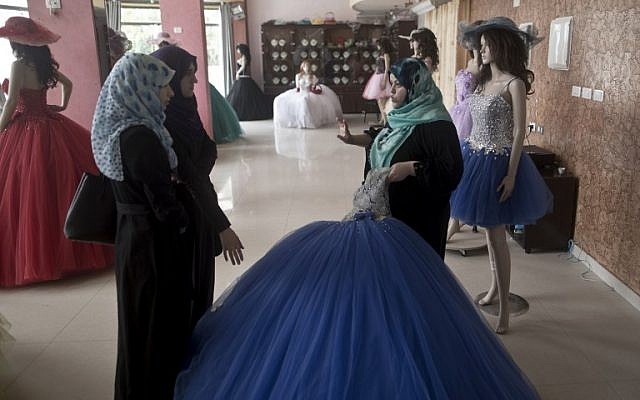 A Palestinian vendor (R) shows a gown to costumers at a shop in Gaza City on April 5, 2016. (AFP PHOTO / MAHMUD HAMS)