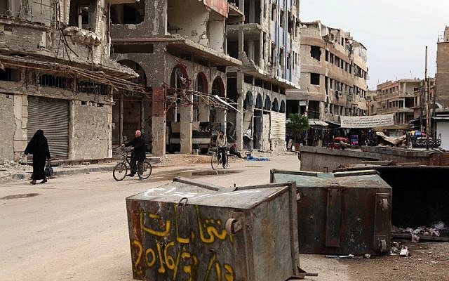 Syrians pass anti-election graffiti on a dust bin in the rebel-held city of Douma on the eastern outskirts of the capital on April 13, 2016, as Syrians in government held areas voted in the parliamentary elections. (AFP/AMER ALMOHIBANY)