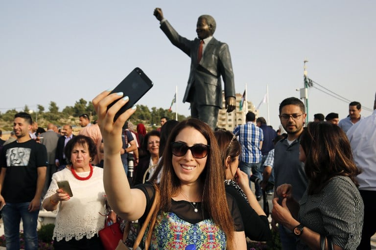 A Palestinian woman takes a selfie in front of a giant statue of Nelson Mandela following its inauguration ceremony in the West Bank city of Ramallah on April 26, 2016. Palestinians inaugurated the statue of Mandela donated by the South African city of Johannesburg to their political capital. The six-metre (20-foot) two-tonne bronze statue was a gift from Johannesburg with which Ramallah is twinned. / AFP PHOTO / ABBAS MOMANI