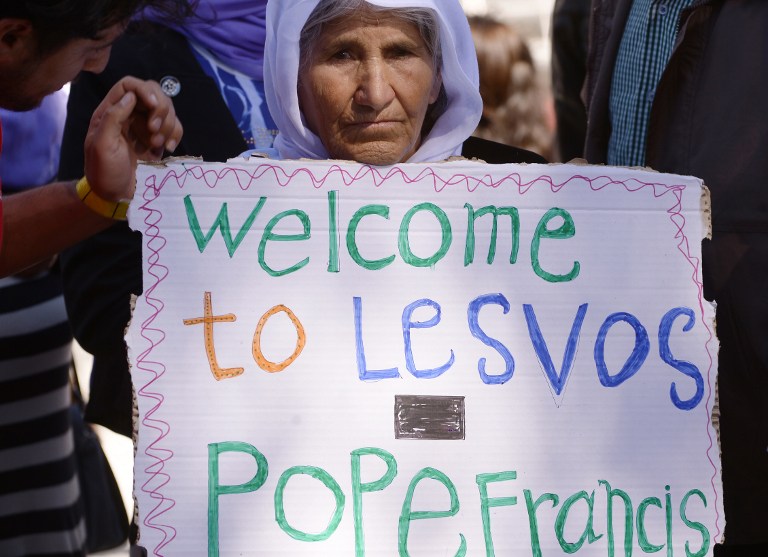 A woman holds a placard reading 'Welcome to Lesbos Pope Francis' on April 16, 2016 at the Moria refugee camp, on the Greek island of Lesbos, prior the arrival of the pontiff. (FILIPPO MONTEFORTE / AFP PHOTO) A woman holds a placard reading 'Welcome to Lesbos Pope Francis' on April 16, 2016 at the Moria refugee camp, on the Greek island of Lesbos, prior the arrival of the pontiff. (FILIPPO MONTEFORTE / AFP PHOTO)