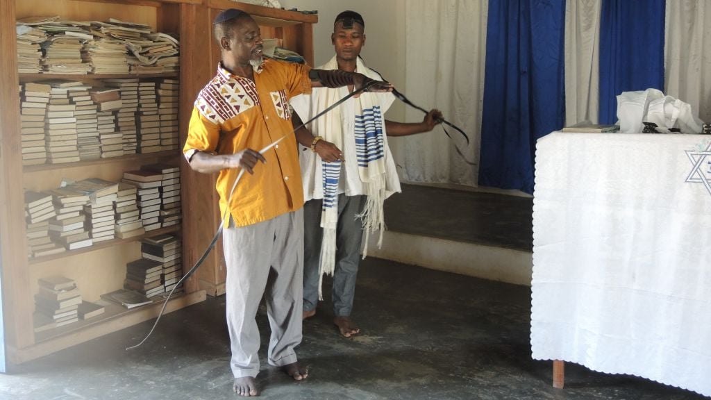 Angel Wilberforce Tetteh, a new member, wraps tefillin for the third time in his life with the assistance of community leader Kofi Kwartengy on February 21, 2016. (Melanie Lidman/Times of Israel)