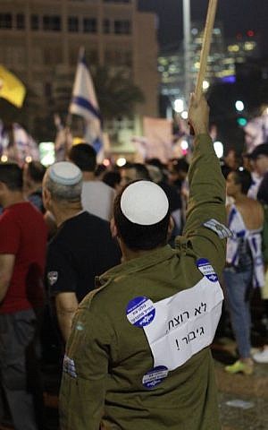 A man with a sign on his shirt reading, 'Not a murderer, a hero,' holds an Israeli flag sign during a rally in Tel Aviv on April 19, 2016 to support Elor Azria, an Israeli soldier recently charged with manslaughter after shooting a prone and wounded Palestinian assailant in the head. (Judah Ari Gross/Times of Israel)
