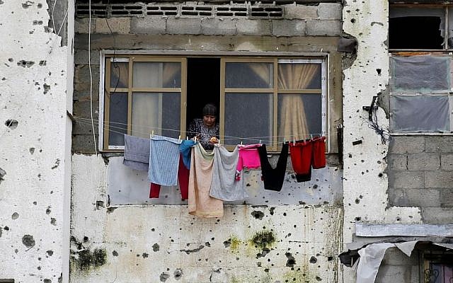 In this Feb. 22, 2016 photo, a Palestinian woman hangs clothes in a section of a damaged apartment block, which was partially destroyed during the 2014 war between Israel and Hamas, in Beit Lahiya, Gaza Strip. (AP Photo/Hatem Moussa, File)
