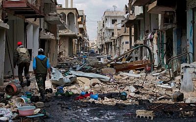 In this April 14, 2016 image, Syrian soldiers walk through a devastated part of the town of Palmyra as families load their belongings onto a bus in the central Homs province, Syria. (AP Photo/Hassan Ammar) 