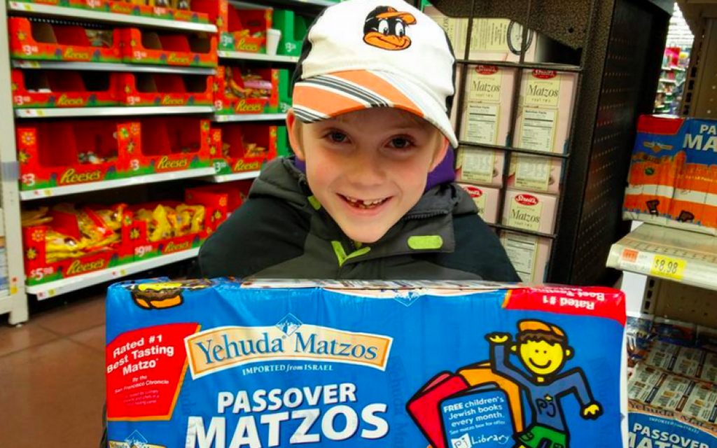 A PJ Library reader hefts a five-pound box of Yehuda Matzos shrink-wrapped with PJ Library material (Courtesy PJ Library Facebook page) A PJ Library reader hefts a five-pound box of Yehuda Matzos shrink-wrapped with PJ Library material (Courtesy PJ Library Facebook page)