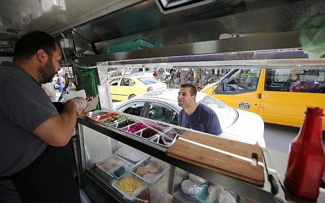 Palestinian al-Barghuti serves food to a customer at his food truck called "Food Train" which he runs with his friend al-Bibi in the West Bank city of Ramallah, May 3, 2016. (AFP/ABBAS MOMANI) Palestinian al-Barghuti serves food to a customer at his food truck called "Food Train" which he runs with his friend al-Bibi in the West Bank city of Ramallah, May 3, 2016. (AFP/ABBAS MOMANI)