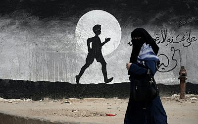 A Palestinian woman walks past a graffiti painted on a wall of the United Nations school of Beit Hanoun, in the northern Gaza Strip, on May 9, 2016. (AFP PHOTO / THOMAS COEX)