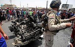 A member of the Iraqi security forces stands guard as civilians look at the damage following a car bomb attack in Sadr City, a Shiite area north of the capital Baghdad, on May 11, 2016. (AFP PHOTO / AHMAD AL-RUBAYE)