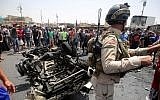 A member of the Iraqi security forces stands guard as civilians look at the damage following a car bomb attack in Sadr City, a Shiite area north of the capital Baghdad, on May 11, 2016. (AFP PHOTO / AHMAD AL-RUBAYE)